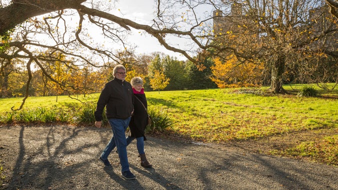Visitors walking in the autumnal grounds of Penrhyn Castle, Wales